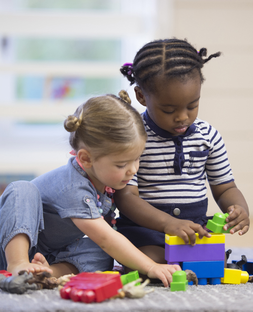 image of two young students playing with building blocks on classroom floor.